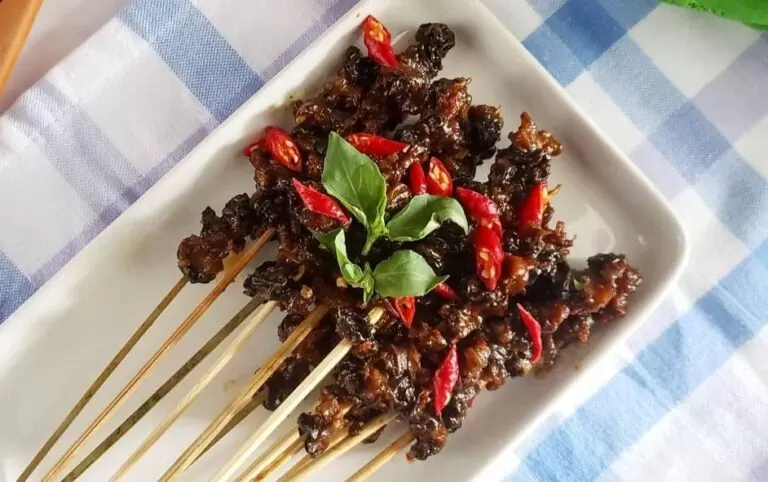 Gambar Sate Kolombi khas Sulawesi Utara yang disajikan dengan bumbu rempah merah, terlihat lezat dan unik dengan tusukan keong rawa yang kenyal